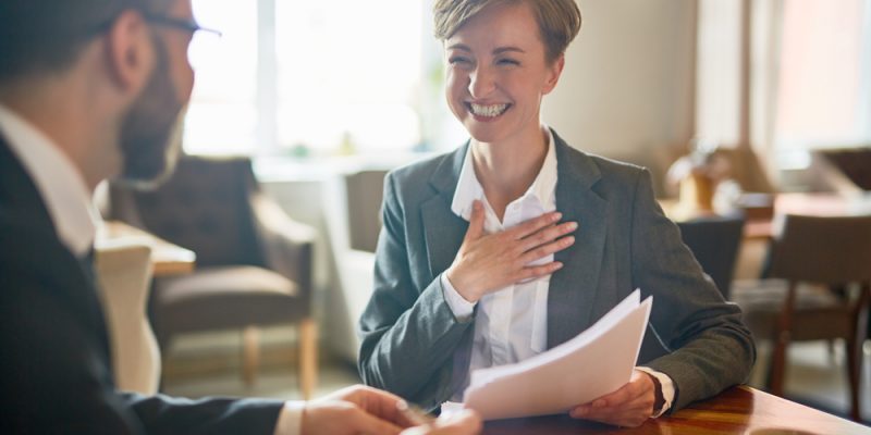 Laughing businesswoman with papers talking to her colleague during meeting in cafe